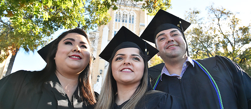 Three graduates in regalia in front of chapel